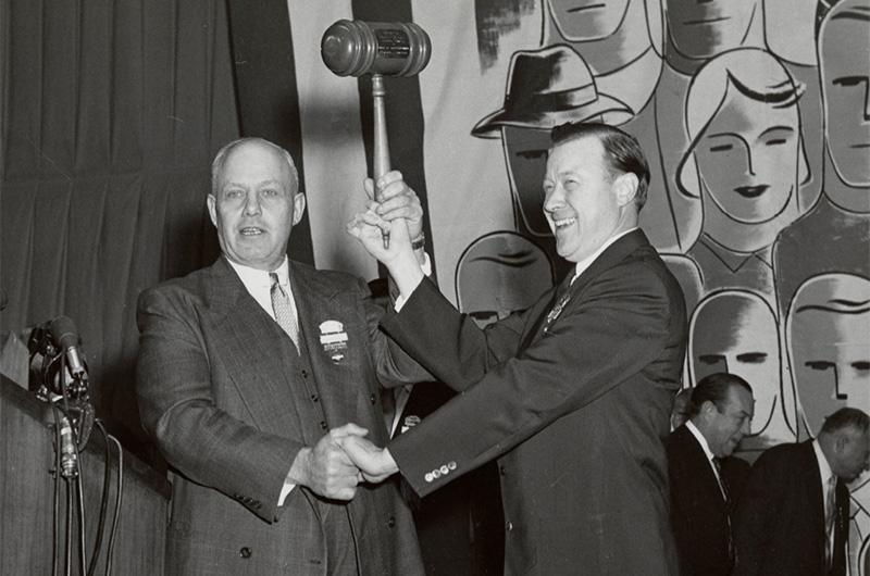 George Meany and Walter Reuther shake hands and raise gavel to commemorate the merger between the AFL and the CIO at the first annual convention of the AFL-CIO in 1955